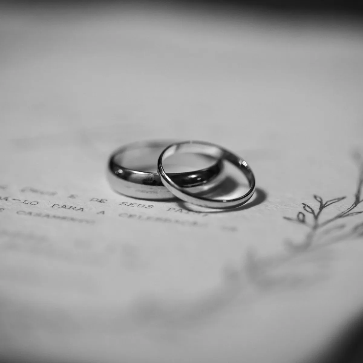 Two wedding bands resting on a cream invitation, in black and white